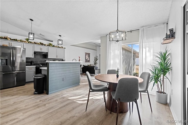 dining area with an inviting chandelier, lofted ceiling, a textured ceiling, and light hardwood / wood-style flooring