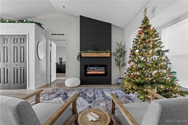 living room featuring hardwood / wood-style floors, lofted ceiling, a fireplace, and a textured ceiling