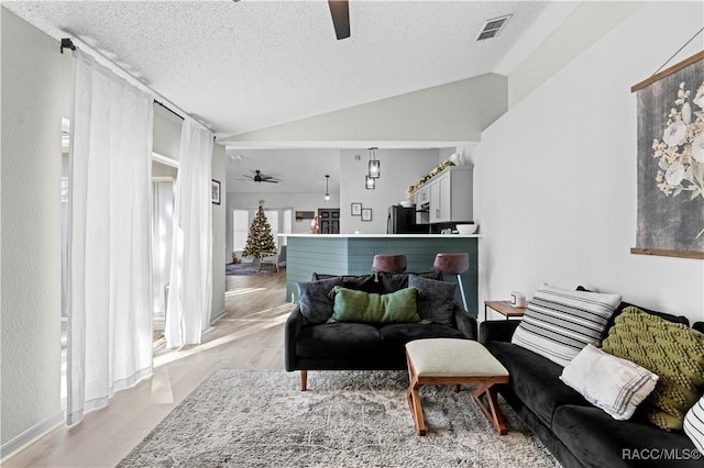 living room with ceiling fan, light wood-type flooring, lofted ceiling, and a textured ceiling