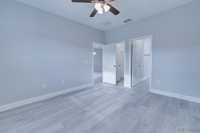 unfurnished bedroom featuring a closet, a walk in closet, ceiling fan, and light hardwood / wood-style flooring