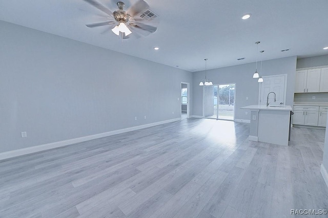 unfurnished living room featuring ceiling fan with notable chandelier, light hardwood / wood-style floors, and sink