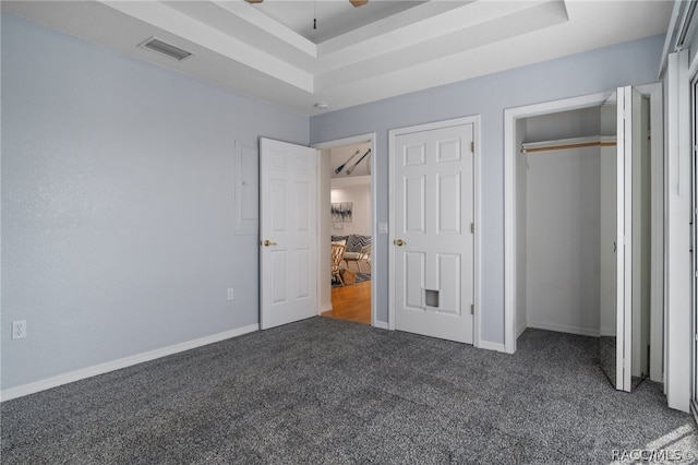 unfurnished bedroom featuring dark colored carpet, a tray ceiling, and ceiling fan