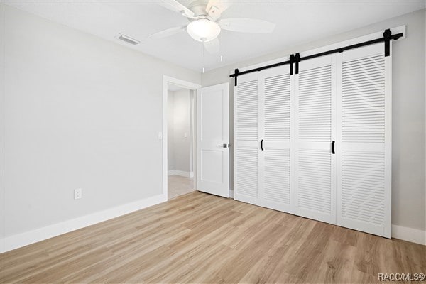 3929 N Sagomon Pt, Crystal River, FL 34428 - unfurnished bedroom with a barn door, light wood-style floors, a closet, and a ceiling fan