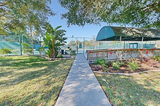 view of property's community with a lawn and tennis court