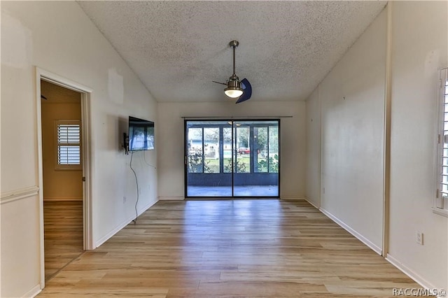 empty room with a textured ceiling, light wood-type flooring, ceiling fan, and lofted ceiling