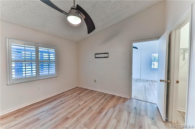 empty room featuring a textured ceiling, light wood-type flooring, a wealth of natural light, and ceiling fan