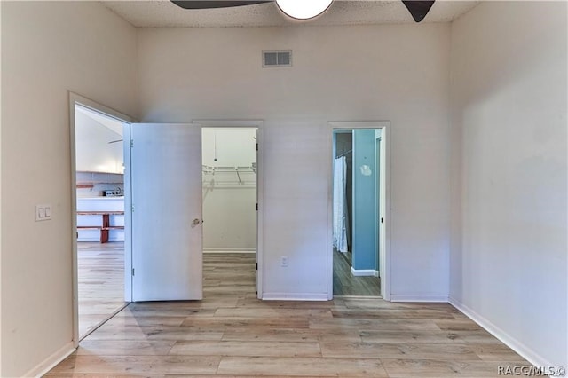 unfurnished bedroom with light wood-type flooring, ceiling fan, a spacious closet, a high ceiling, and a closet