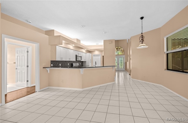 kitchen featuring white cabinets, decorative backsplash, decorative light fixtures, kitchen peninsula, and a breakfast bar area