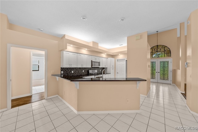 kitchen featuring french doors, tasteful backsplash, kitchen peninsula, a kitchen bar, and white cabinets