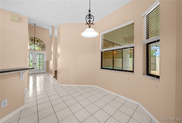 tiled empty room featuring a wealth of natural light, french doors, and a notable chandelier