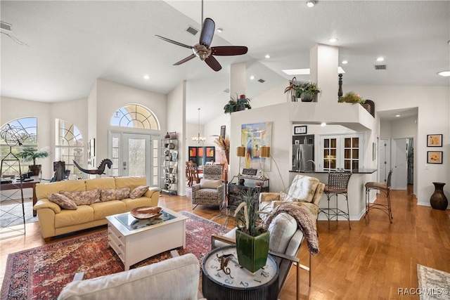 living room featuring ceiling fan with notable chandelier, wood-type flooring, high vaulted ceiling, and french doors