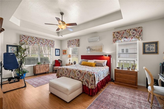 bedroom with wood-type flooring, radiator, a wall mounted air conditioner, and a tray ceiling