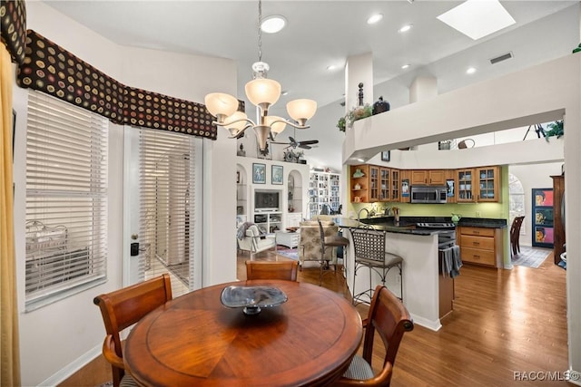 dining space with wood-type flooring, high vaulted ceiling, an inviting chandelier, and a skylight