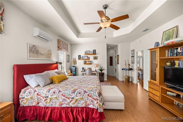 bedroom featuring a raised ceiling, an AC wall unit, hardwood / wood-style floors, and ceiling fan