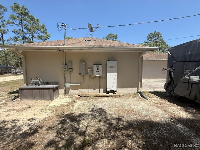 back of house with a shingled roof and stucco siding