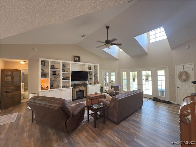 living area with high vaulted ceiling, a stone fireplace, a ceiling fan, a skylight, and visible vents