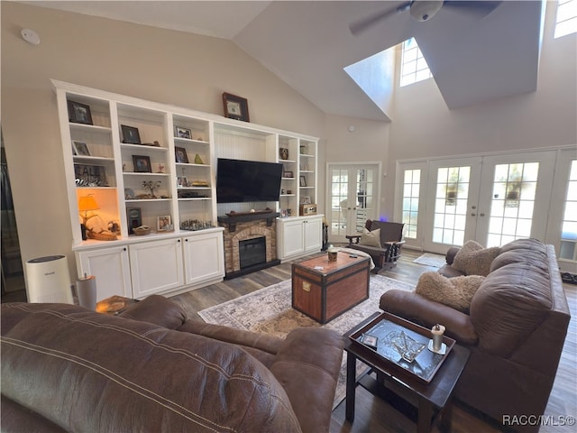 living room with ceiling fan, french doors, a stone fireplace, a skylight, and wood finished floors