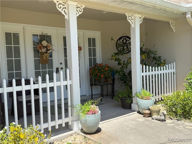 view of exterior entry with stucco siding, covered porch, and fence