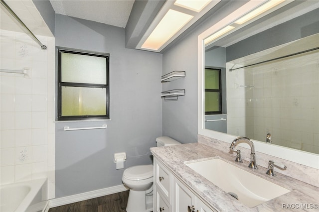 full bathroom with hardwood / wood-style floors, vanity, tiled shower / bath, toilet, and a textured ceiling