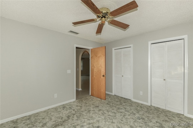 unfurnished bedroom with multiple closets, ceiling fan, light colored carpet, and a textured ceiling