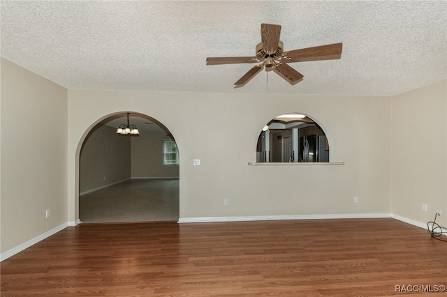 spare room featuring ceiling fan with notable chandelier, dark wood-type flooring, and a textured ceiling