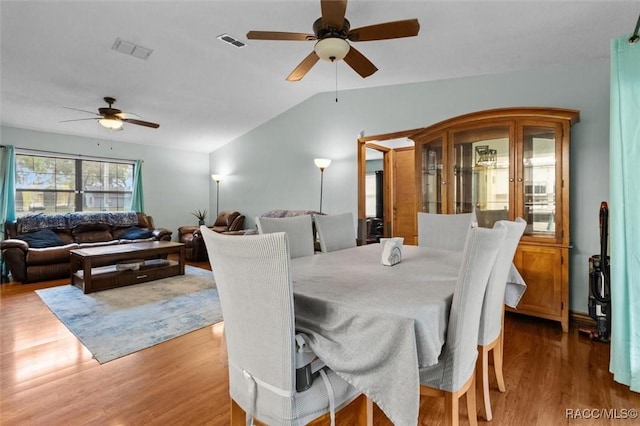 dining room with ceiling fan, visible vents, vaulted ceiling, and wood finished floors