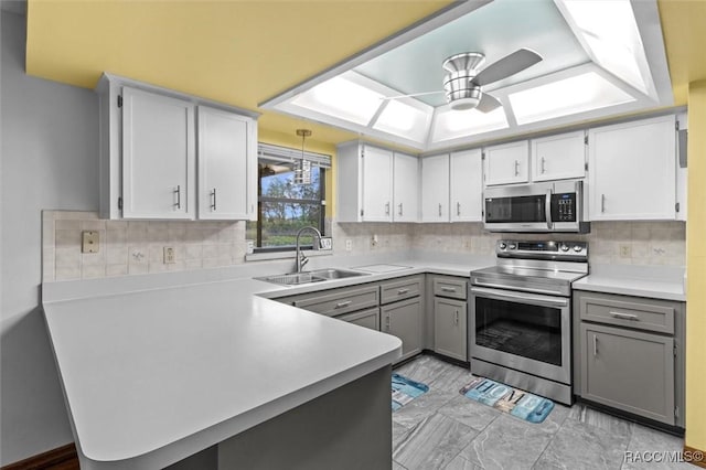 kitchen with ceiling fan, stainless steel appliances, a peninsula, a sink, and light countertops