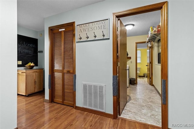 hall with a textured ceiling, wood finished floors, visible vents, and baseboards