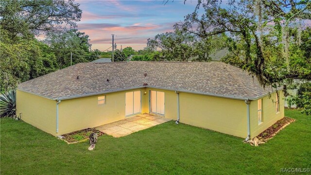3143 Grayton Dr, Spring Hill, FL 34609 - back of property at dusk with stucco siding, a shingled roof, and a lawn