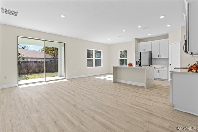 kitchen with appliances with stainless steel finishes, a center island with sink, white cabinetry, and light hardwood / wood-style flooring