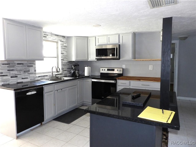 kitchen with appliances with stainless steel finishes, tasteful backsplash, white cabinetry, sink, and light tile patterned floors