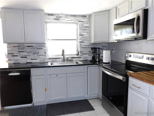 kitchen with appliances with stainless steel finishes, tasteful backsplash, sink, white cabinets, and light tile patterned floors