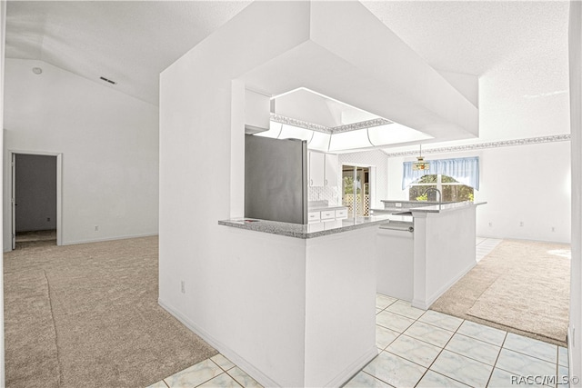 kitchen featuring stainless steel refrigerator, kitchen peninsula, a textured ceiling, light carpet, and white cabinets