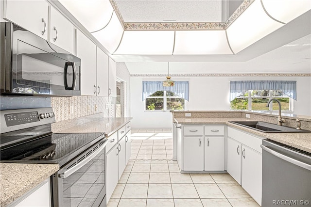 kitchen with appliances with stainless steel finishes, sink, light tile patterned floors, white cabinetry, and hanging light fixtures