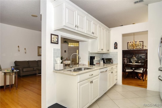 kitchen with tasteful backsplash, sink, a notable chandelier, dishwasher, and white cabinetry