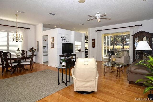 living room featuring ceiling fan with notable chandelier and light hardwood / wood-style flooring