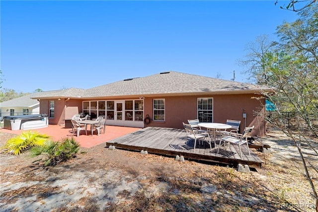 back of house with a hot tub, stucco siding, outdoor dining area, and a deck