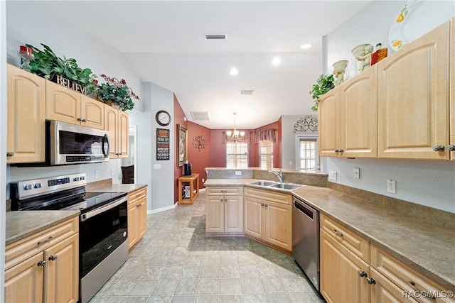 kitchen with a peninsula, a sink, light brown cabinetry, stainless steel appliances, and vaulted ceiling