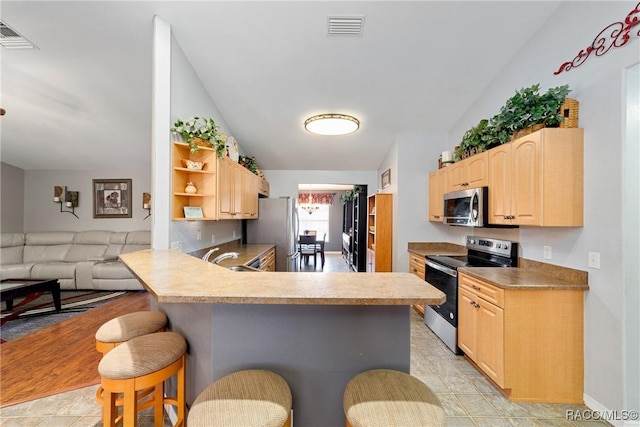 kitchen with light brown cabinetry, visible vents, a kitchen bar, vaulted ceiling, and stainless steel appliances