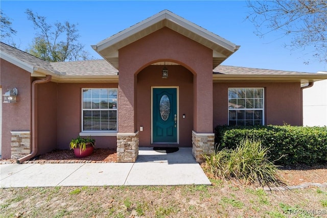 entrance to property with a shingled roof, stucco siding, and stone siding