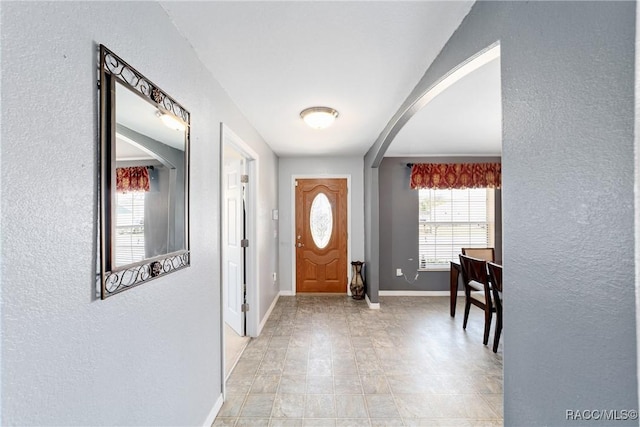 entrance foyer with arched walkways, baseboards, and a textured wall