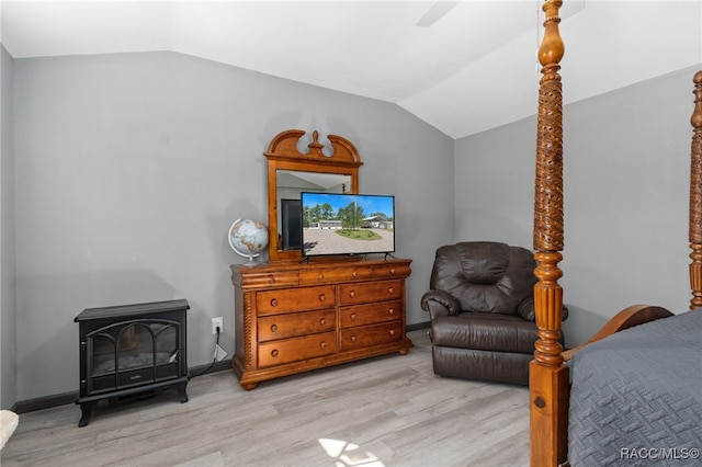 bedroom featuring a wood stove, ceiling fan, vaulted ceiling, and light wood-type flooring