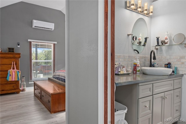 bathroom featuring hardwood / wood-style floors, vanity, a wall unit AC, and vaulted ceiling