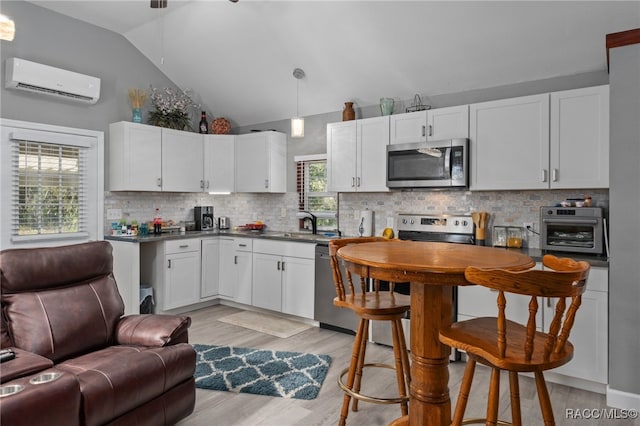 kitchen with tasteful backsplash, stainless steel appliances, a wall mounted AC, white cabinetry, and hanging light fixtures