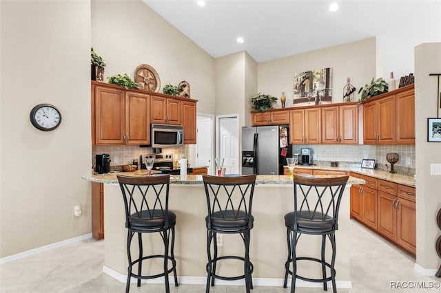 kitchen featuring light stone countertops, a breakfast bar, stainless steel appliances, a high ceiling, and an island with sink