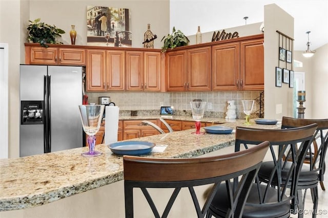 kitchen featuring stainless steel fridge, backsplash, a kitchen breakfast bar, light stone counters, and pendant lighting