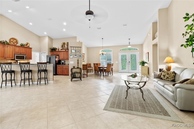 tiled living room with french doors, ceiling fan with notable chandelier, and a high ceiling