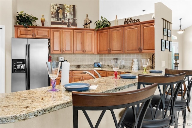 kitchen with stainless steel fridge, a kitchen breakfast bar, tasteful backsplash, light stone counters, and hanging light fixtures