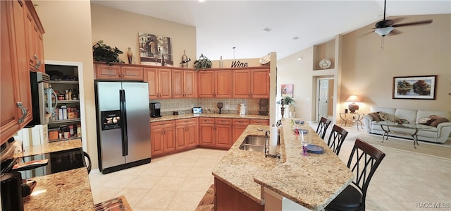 kitchen with light stone countertops, backsplash, a breakfast bar, stainless steel appliances, and ceiling fan