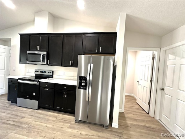 kitchen with lofted ceiling, stainless steel appliances, light hardwood / wood-style floors, and a textured ceiling